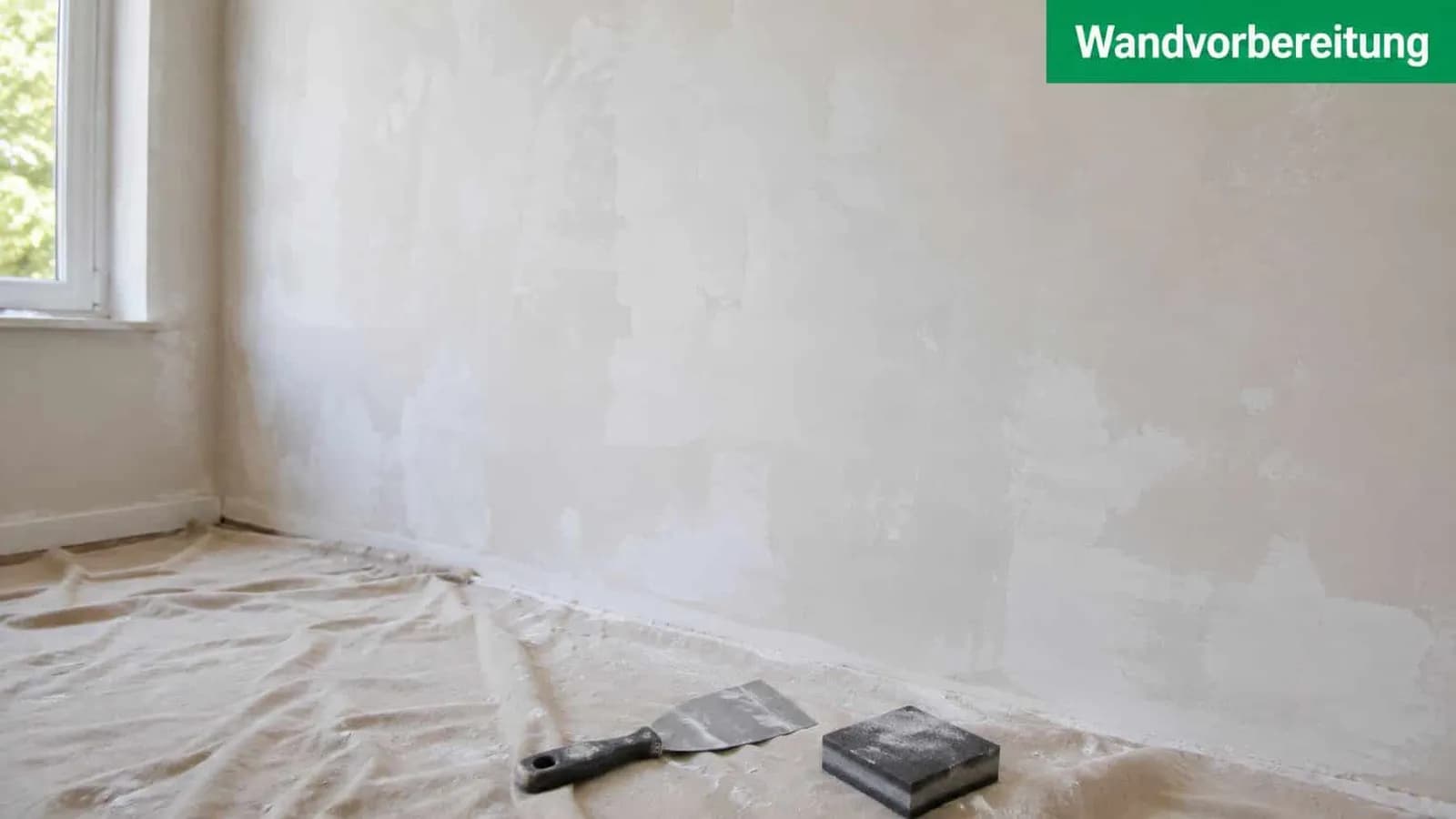 Ein Raum mit einer frisch verputzten Wand und Werkzeugen zur Wandvorbereitung auf dem Boden.