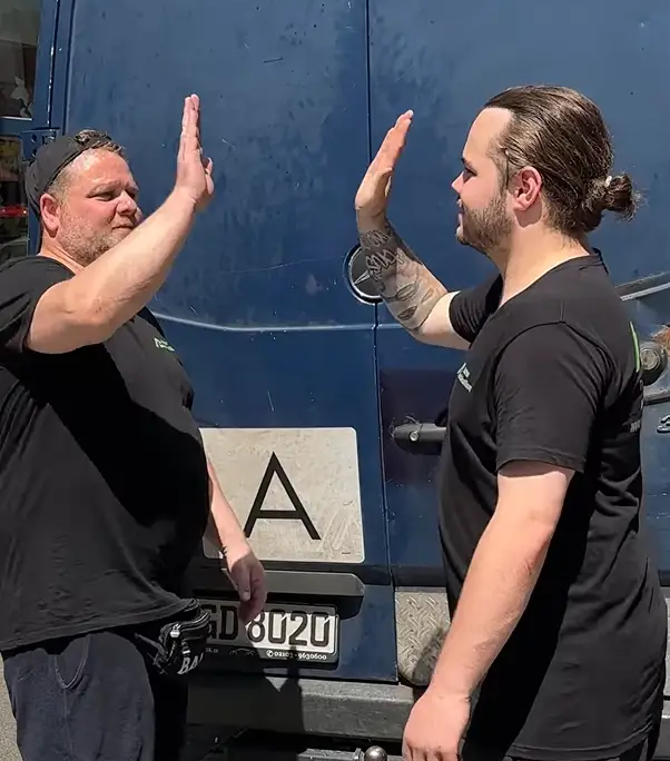Zwei Mitarbeiter von NRW Haushaltsauflösung beim High-Five vor dem Transporter.