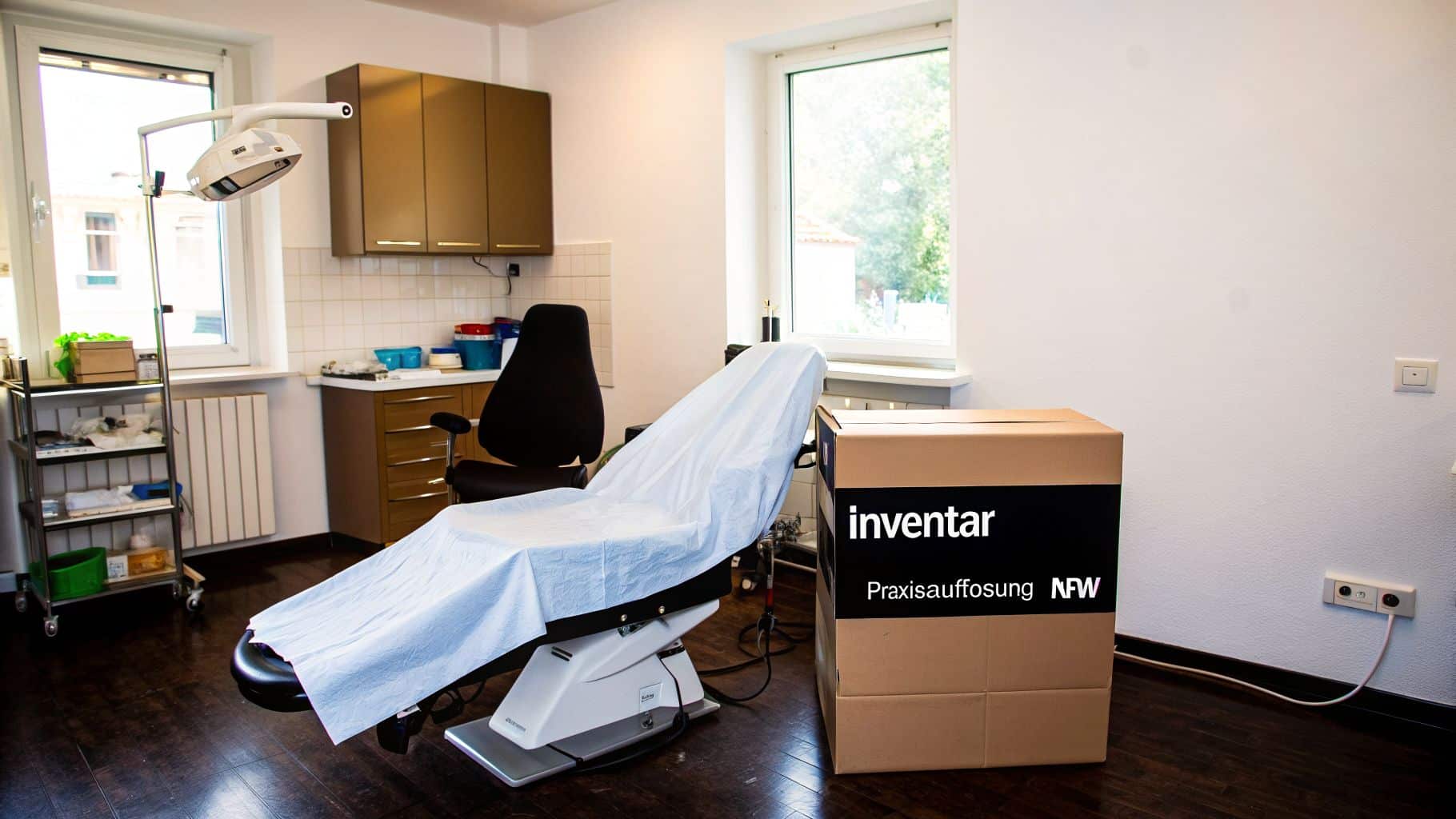 Zahnarztpraxis mit Behandlungsstuhl, Schränken und Umzugskartons, deutet auf Praxisauflösung hin.