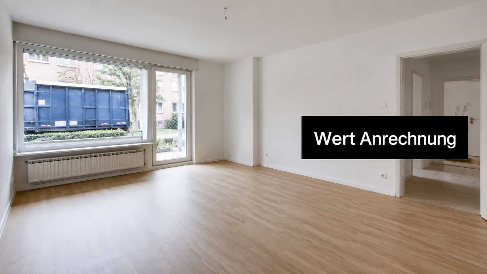 Ein helles, leeres Zimmer mit weiß gestrichenen Wänden, Holzboden, großem Fenster und offener Tür zur Wohnung.
