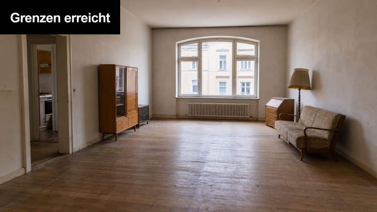 Ein helles, geräumiges Zimmer mit Holzboden, einigen Möbelstücken und einem großen Fenster mit Blick nach draußen.