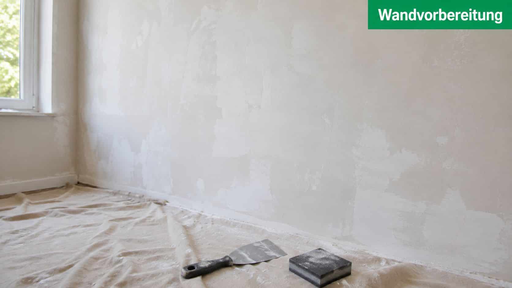 Ein Raum mit einer frisch verputzten Wand und Werkzeugen zur Wandvorbereitung auf dem Boden.